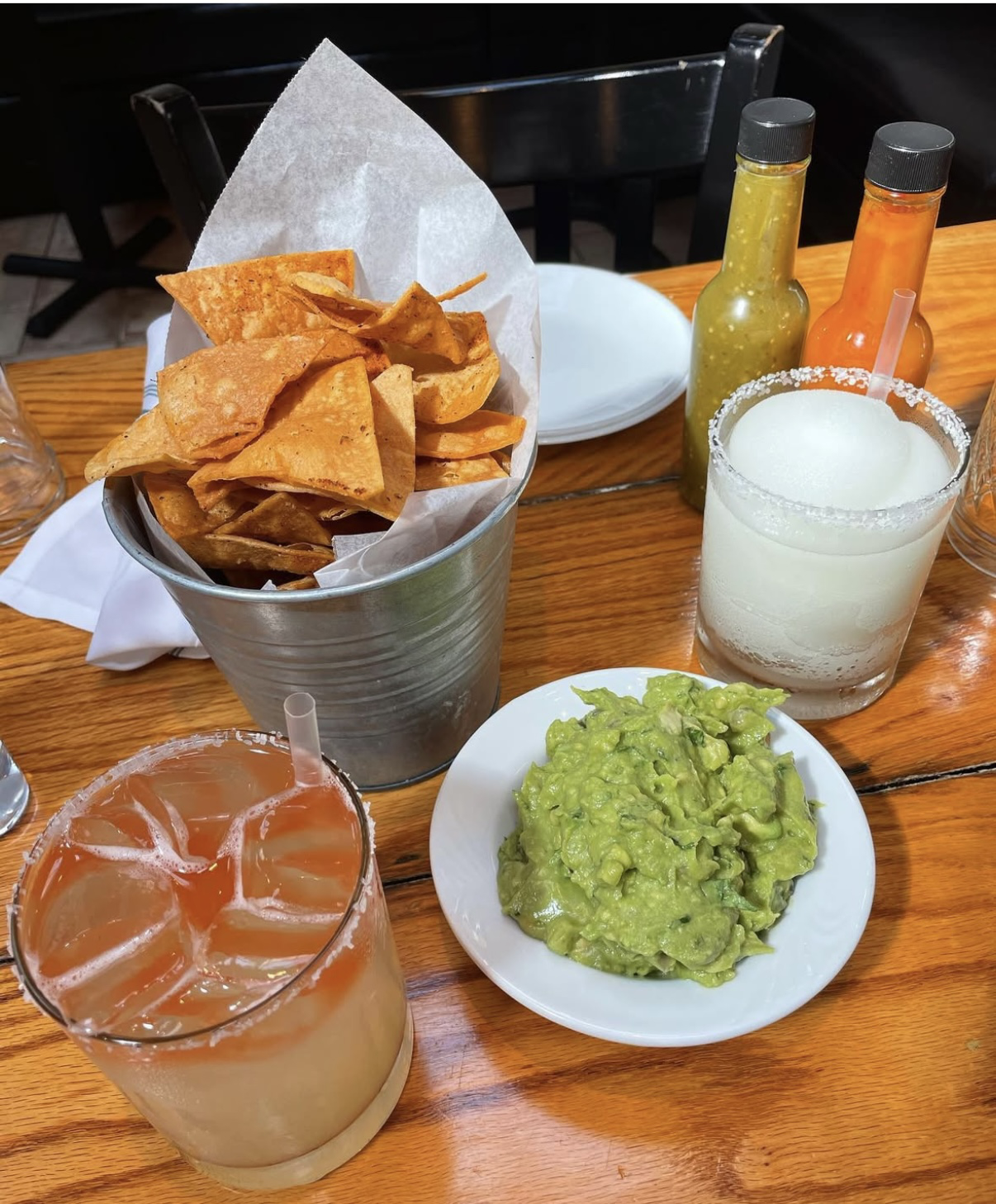 Spread of Guacamole and chips, hot sauces, a frozen margarita, and our spicy margarita